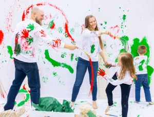 Playful paint splash photo session with family against white wall with red and green handprints. Orlando, Florida