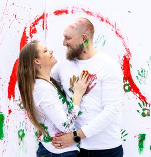 Couple covered in colorful paint embracing against wall decorated with handprints. Orlando, Florida