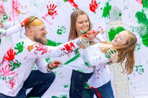 Family playing with paint and making messy art together against white wall with handprints. Orlando, Florida