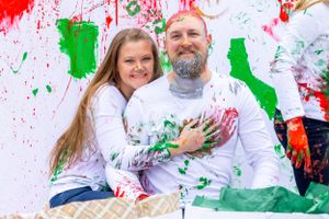 Couple sitting together covered in red and green paint against decorated white wall. Orlando, Florida