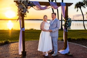 Couple poses under decorated arch at sunset waterfront wedding ceremony. Merritt Island, Florida