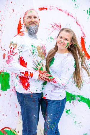 Couple posing with paint-covered hands against wall with festive handprint decorations. Orlando, Florida