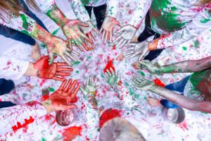 Overhead view of hands forming circle on white surface covered in red and green paint handprints.  Orlando, Florida