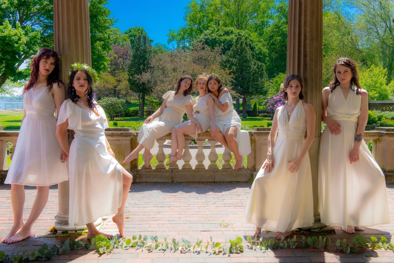 A group in flowing white dresses poses elegantly on outdoor stone steps with decorative bunting.
