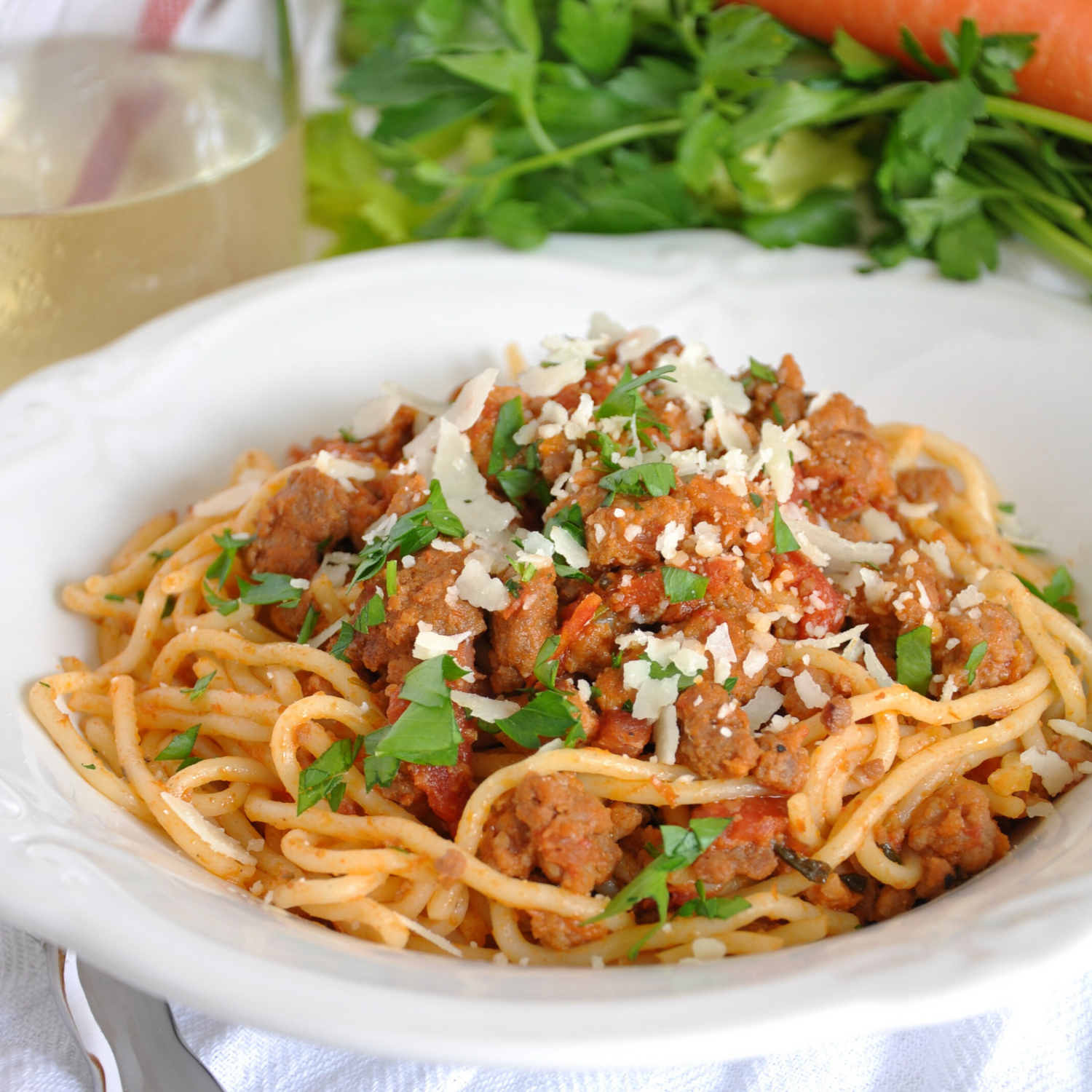 Spaghetti with meat sauce garnished with fresh herbs and shredded cheese on a white plate.