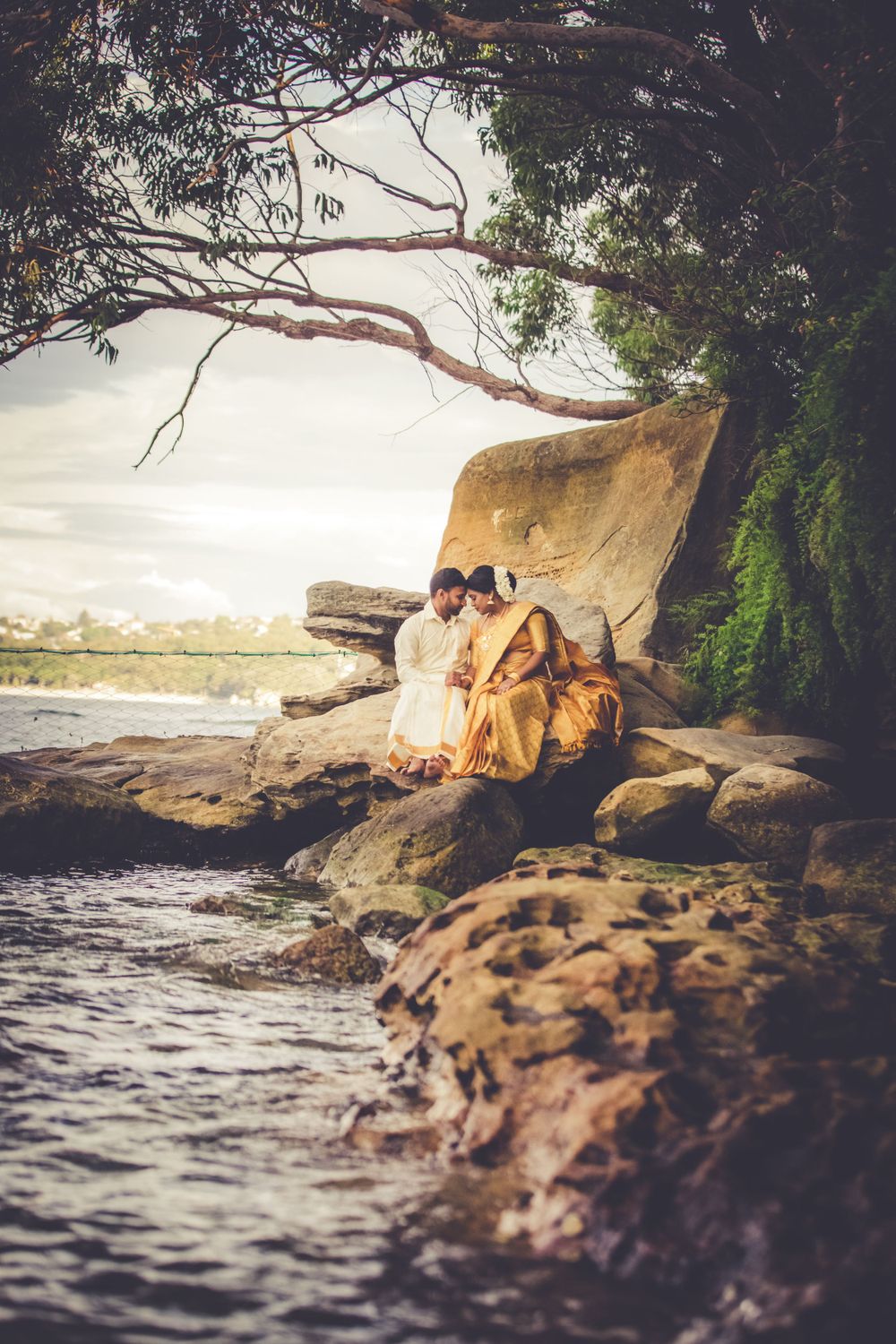 Pre Wedding shoot of a Sri Lankan Tamil couple sitting on some rocks at the edge of the water in Sydney