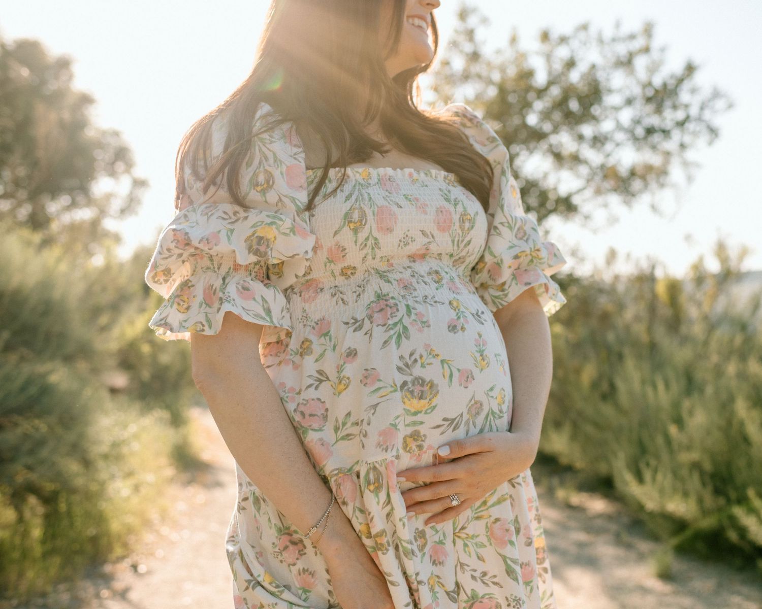 Sunset portrait of someone in a floral dress holding their pregnant belly during maternity photoshoot in San Diego.