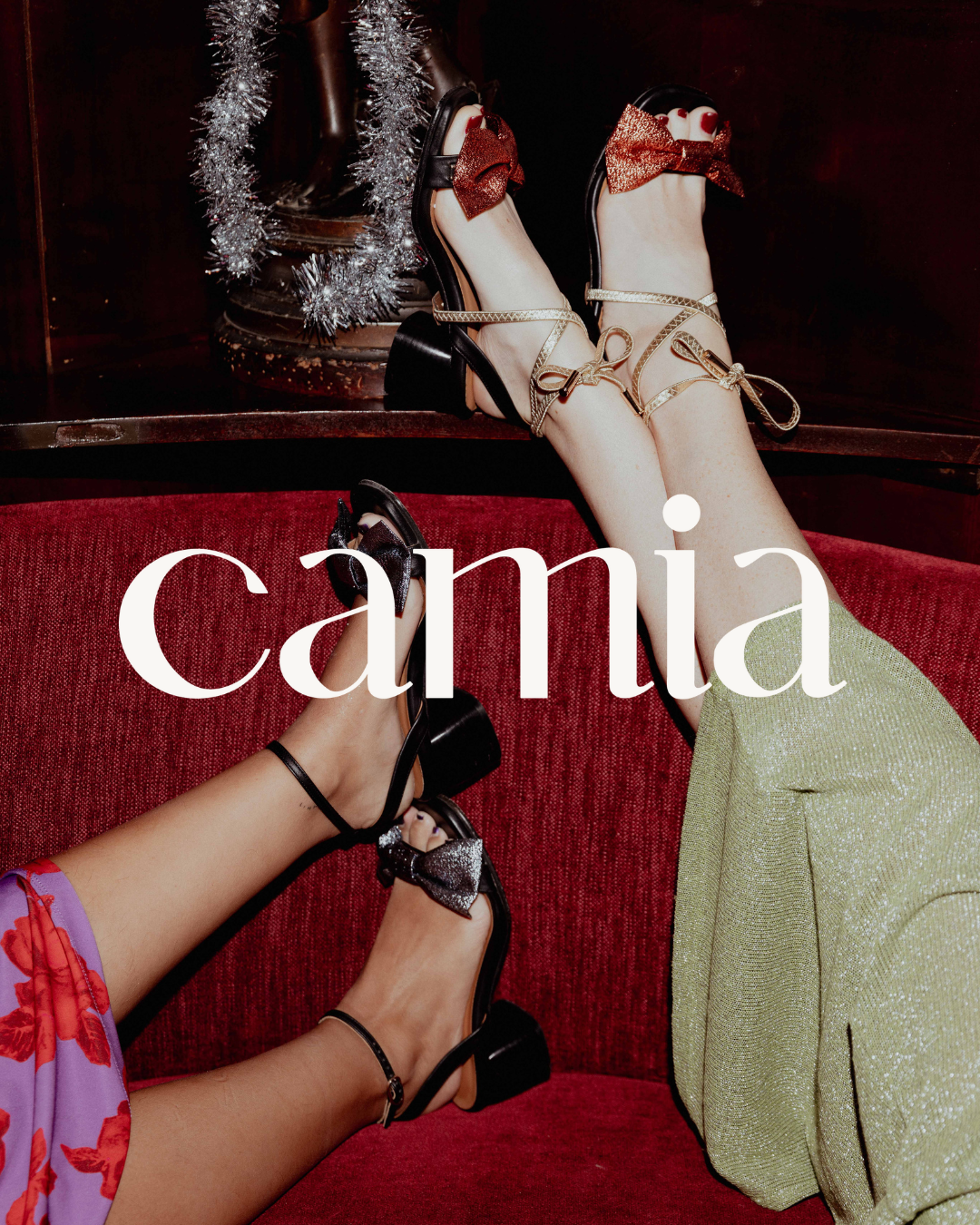 Festive holiday shoes and decorative tinsel with Camia text overlay on red velvet background.