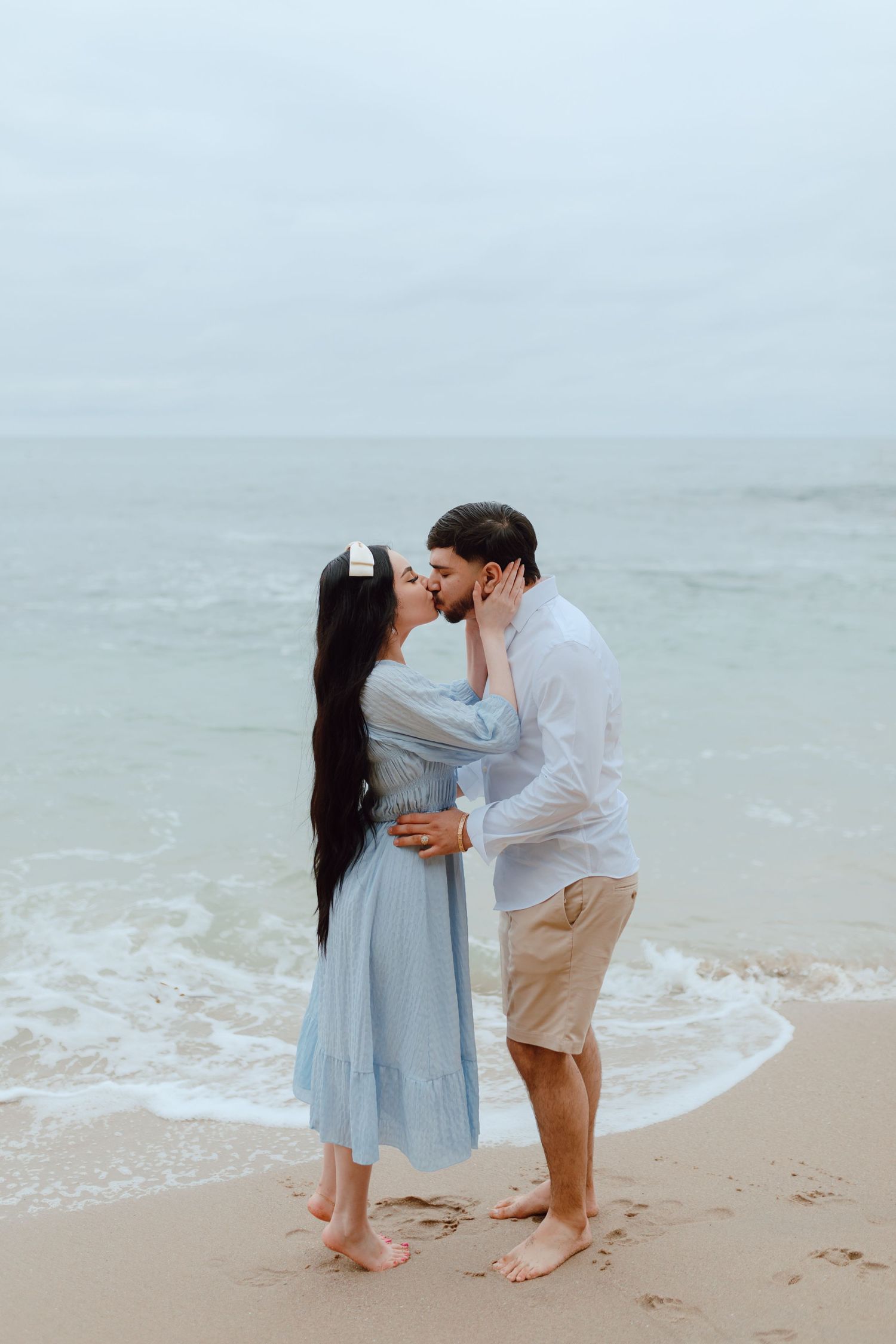 Romantic couple embracing on misty beach with waves rolling in behind them.