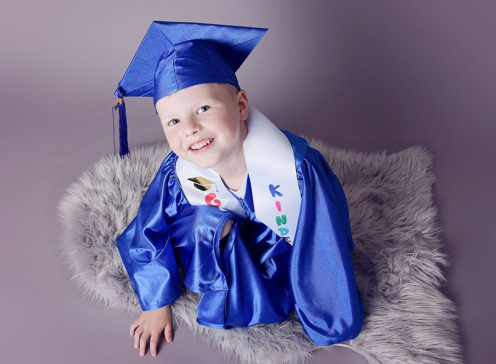 Nursery graduation image in blue cap and gown. Studio lighting on a grey furry rug and on a grey backdrop.