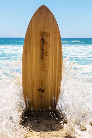 Wooden surfboard standing upright in splashing ocean waves at the beach.