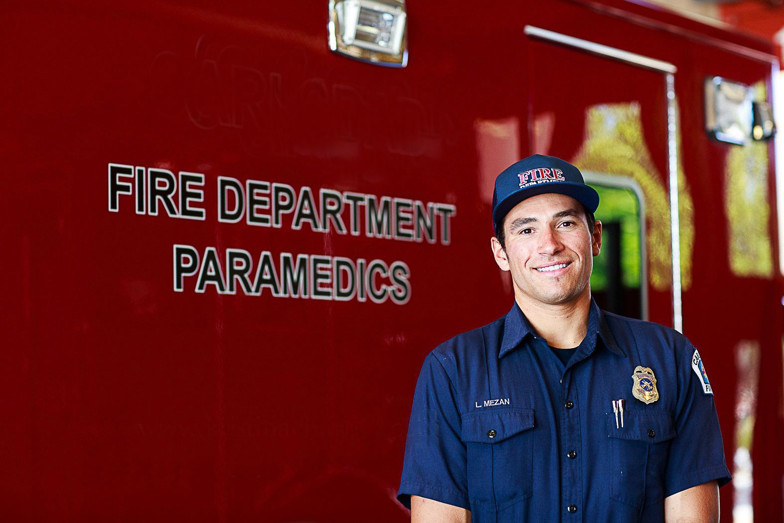Paramedic in navy uniform smiling in front of fire department vehicle.