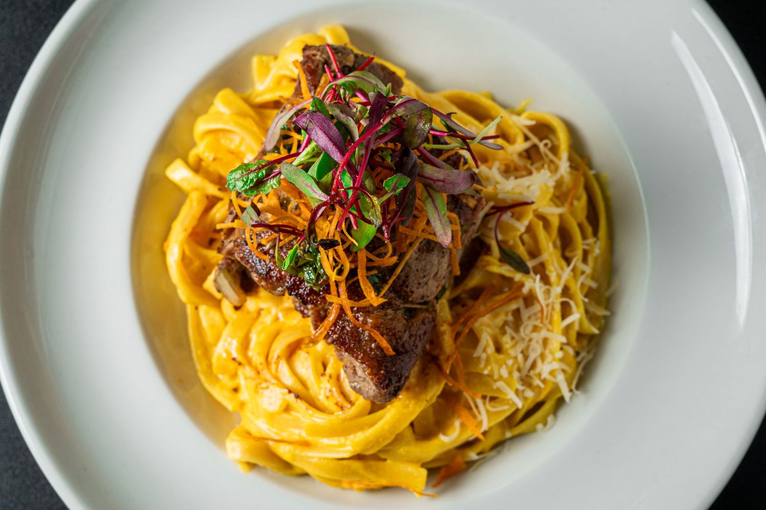 Golden pasta noodles topped with tender braised meat, colorful vegetables and fresh herbs served on a white plate.