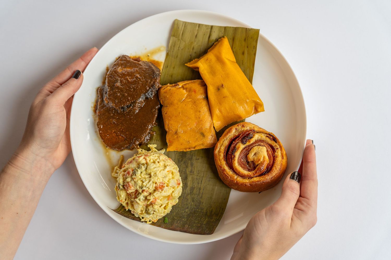 Hands holding white plates with traditional Southern dishes including cornbread and roasted vegetables.