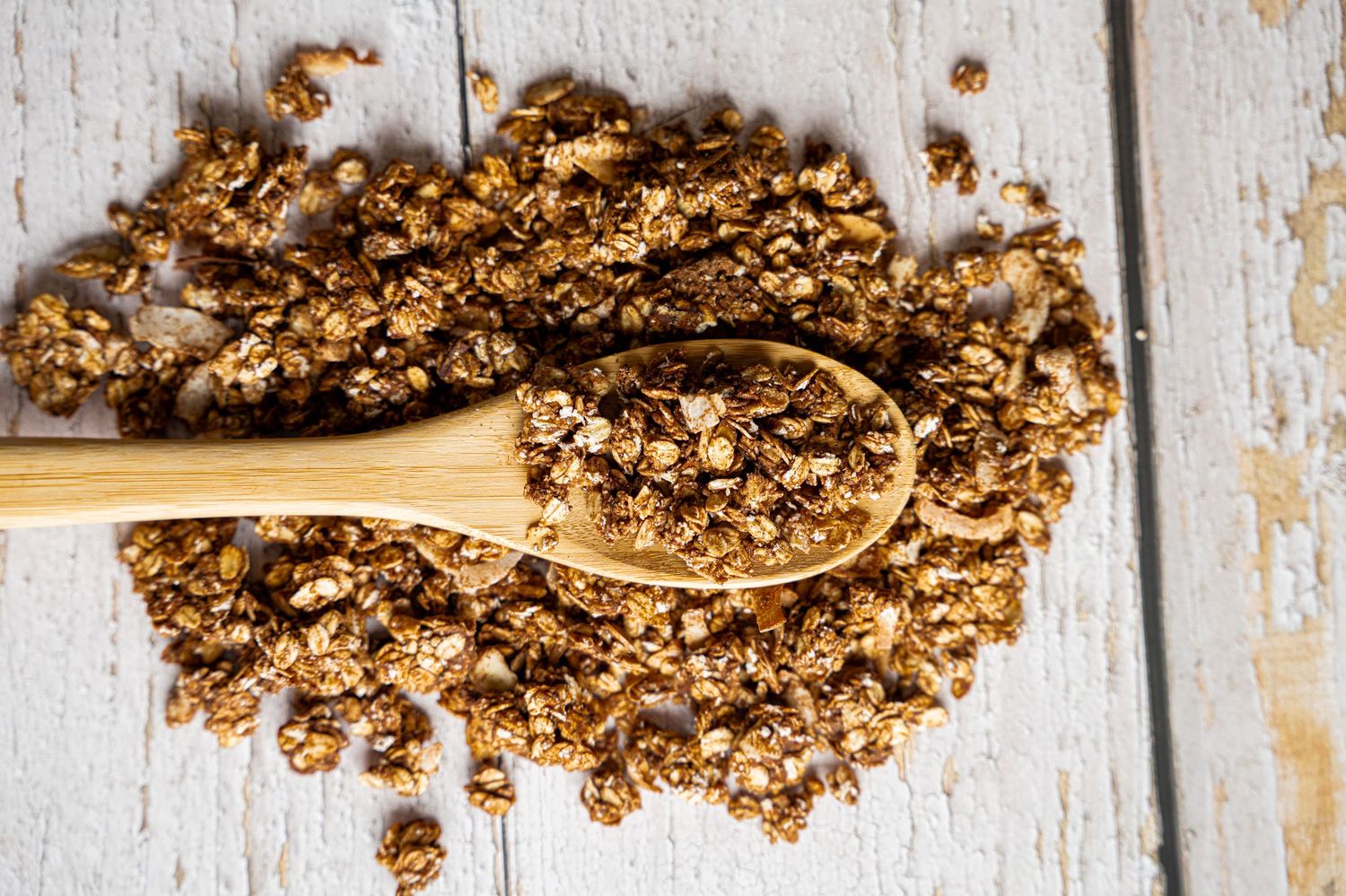 Granola clusters with nuts and dried fruits scattered on a rustic white wooden surface.