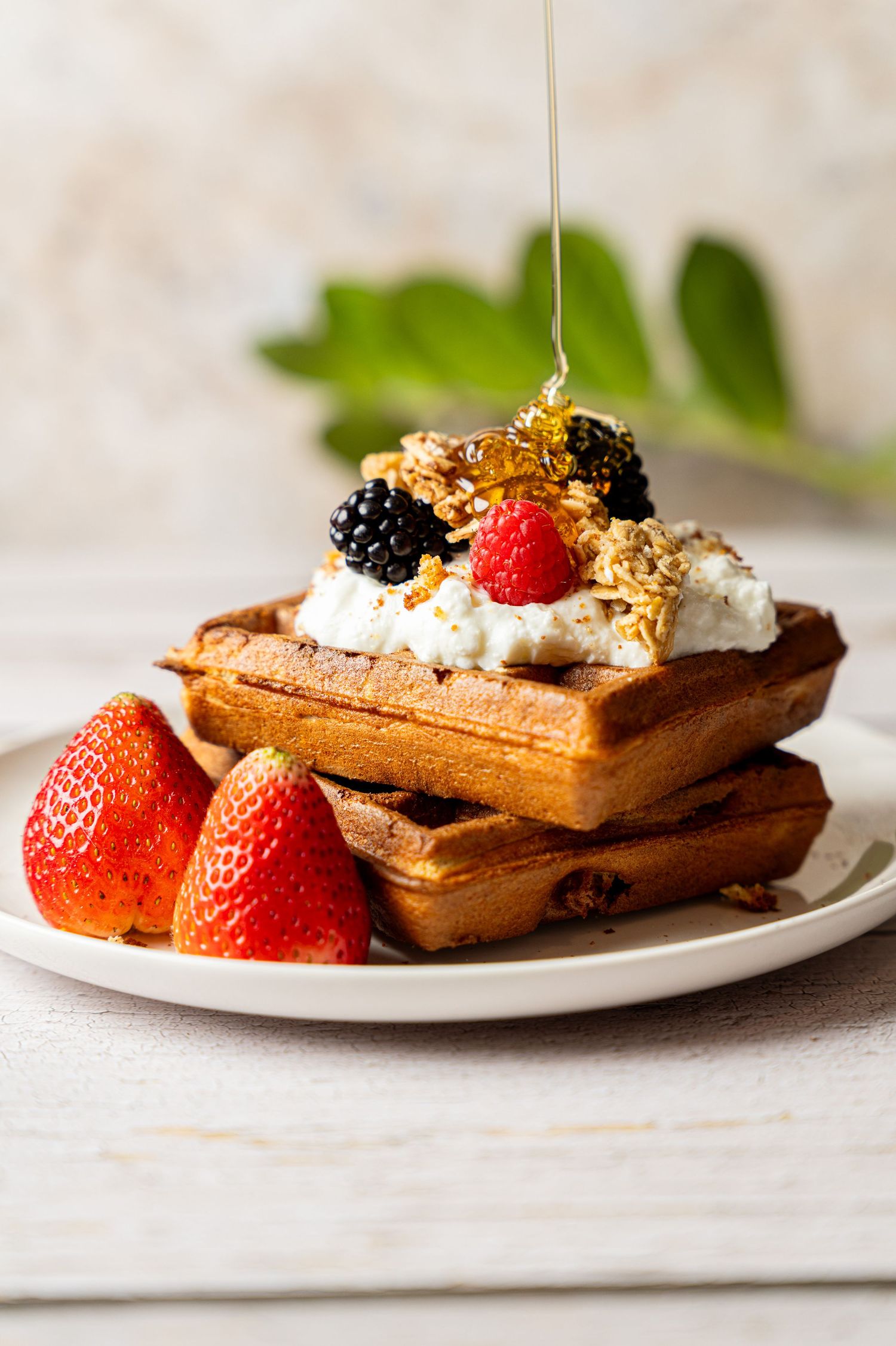 Homemade waffles topped with fresh berries, whipped cream and granola served on white plates in a three-image sequence.