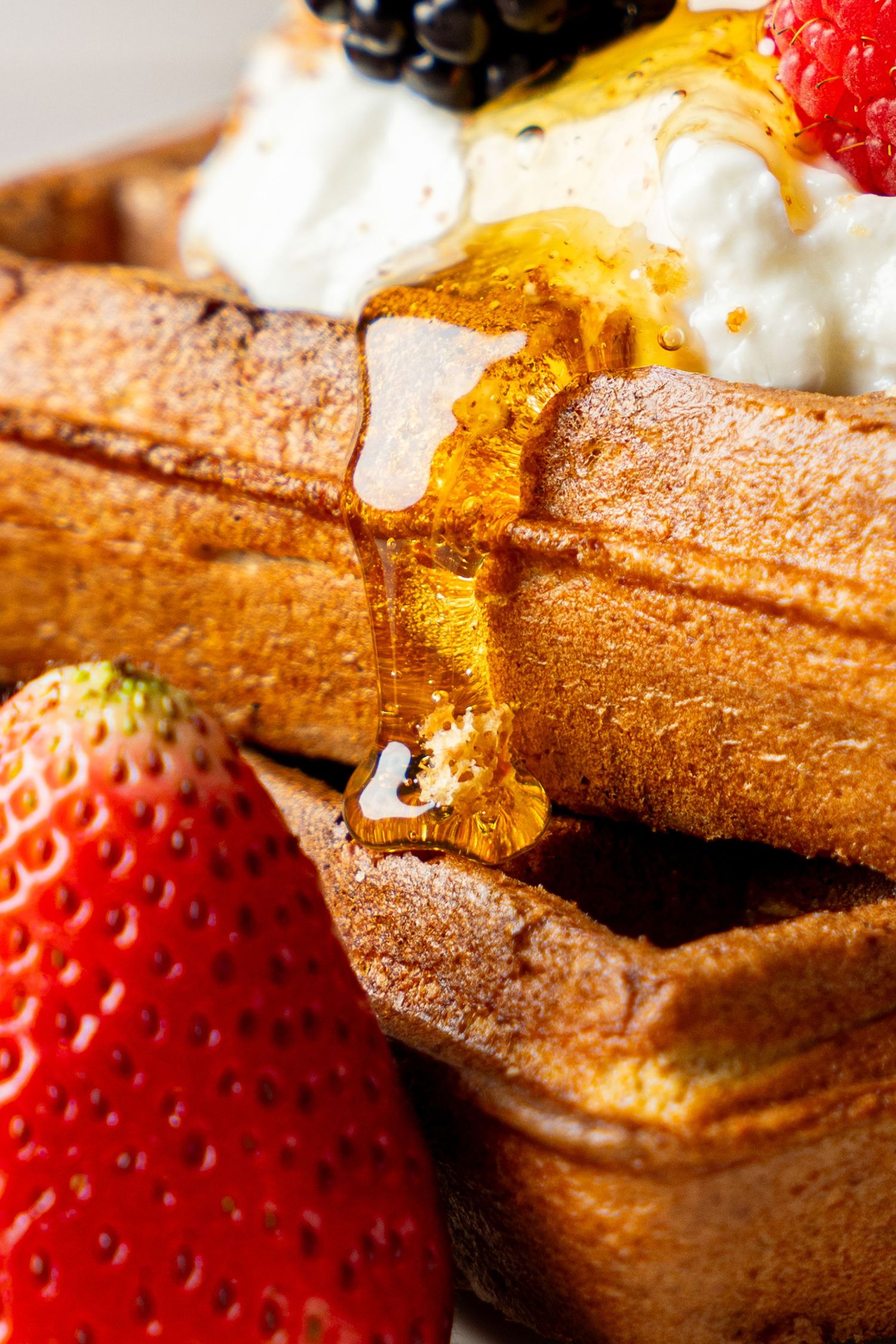 Close-up shot of fresh strawberries and whipped cream on a cinnamon-dusted waffle with golden syrup drizzle.