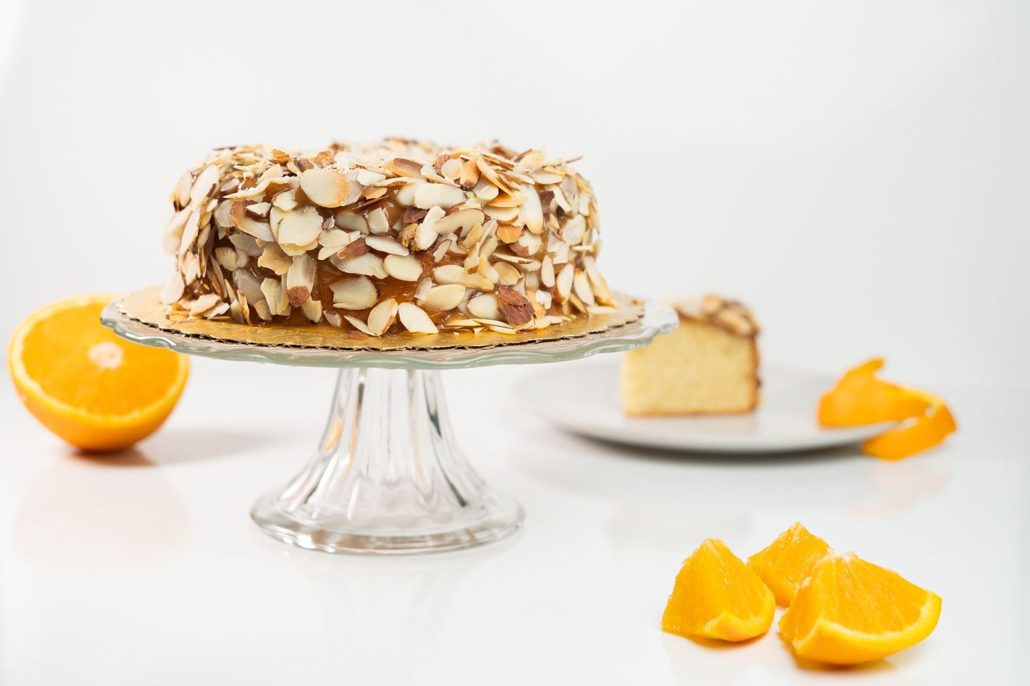 Almond-covered cake on glass stand with orange slices.