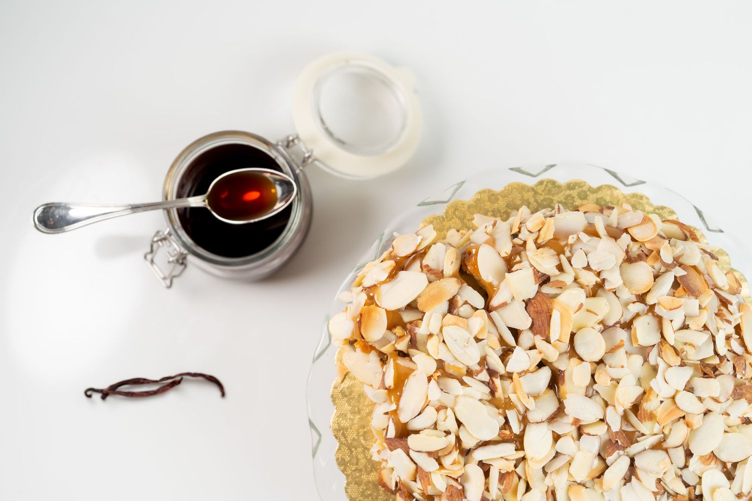 Almond-topped pie with syrup in a small jar on white background.