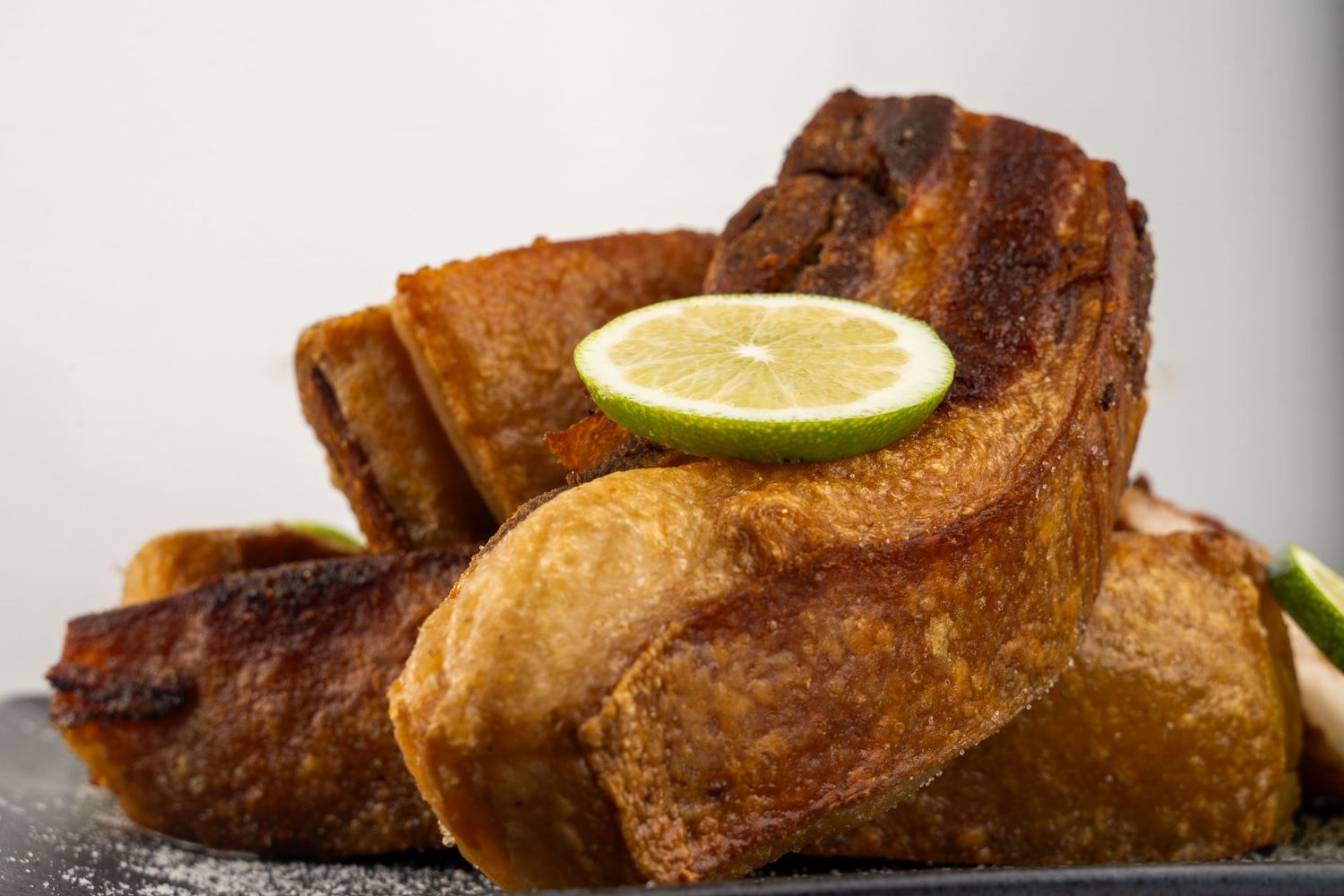 Crispy golden brown chicharron slices stacked with a fresh lime garnish on dark surface.