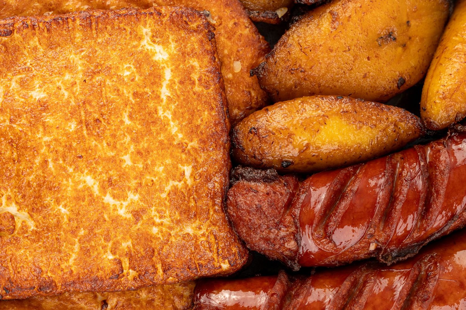 Close-up of golden fried cheese, fried plantains and sausages with crispy texture.