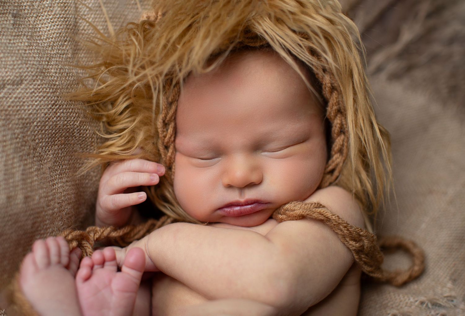Sleeping newborn with yarn wig styled for artistic portrait.