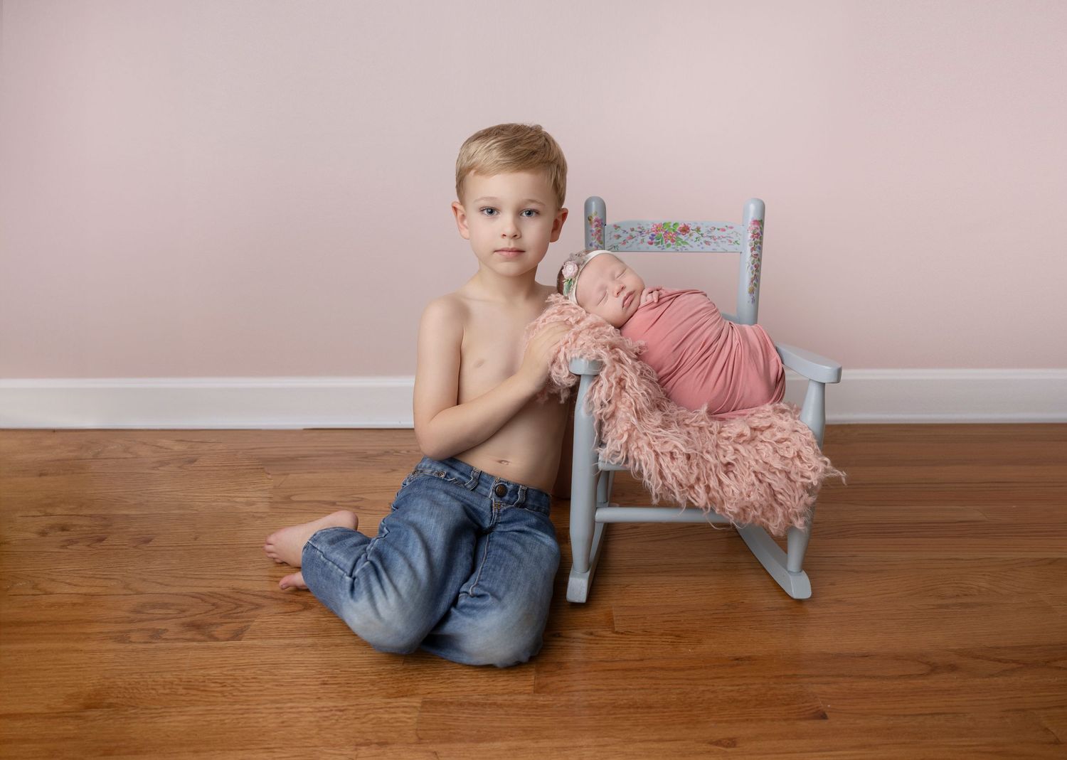 Child sitting next to small chair holding pink cloth against pink wall.