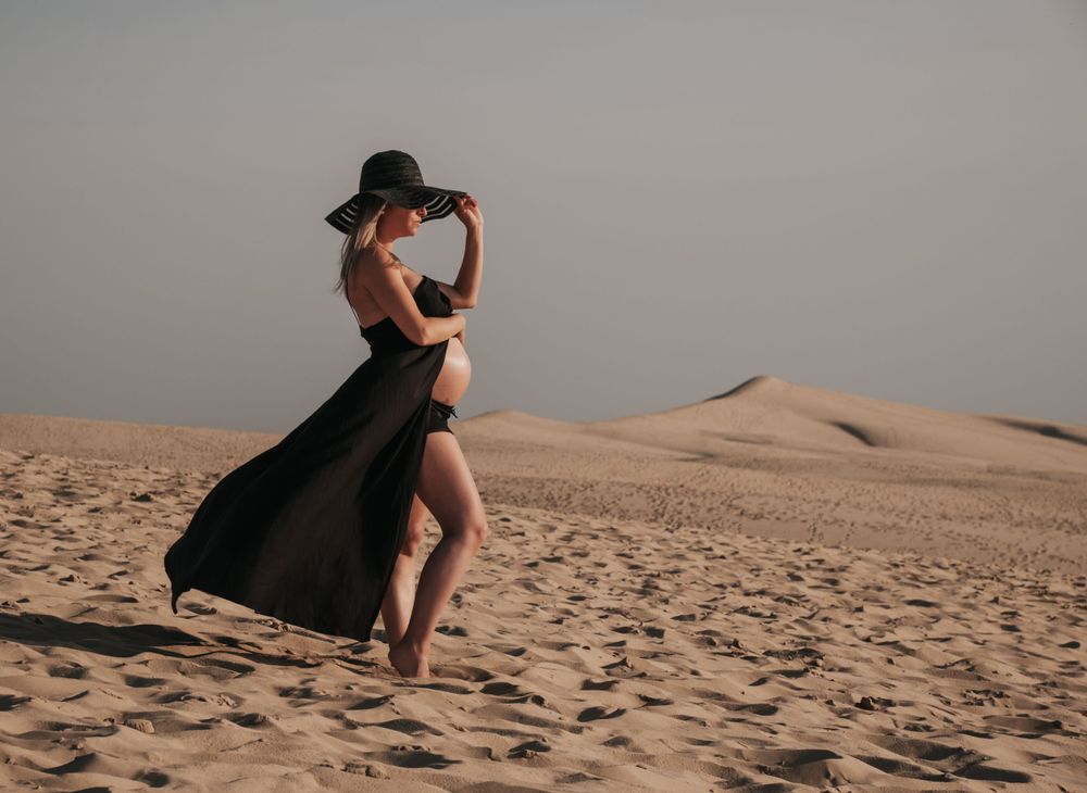 Woman in flowing black dress dancing on sand dunes at sunset. photographe futur maman Bordeaux gironde