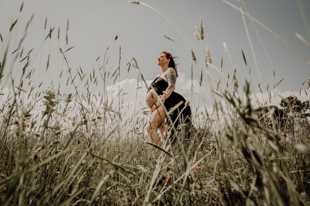 Figure sitting in tall grass with dramatic natural lighting. photographe futur maman Bordeaux gironde
