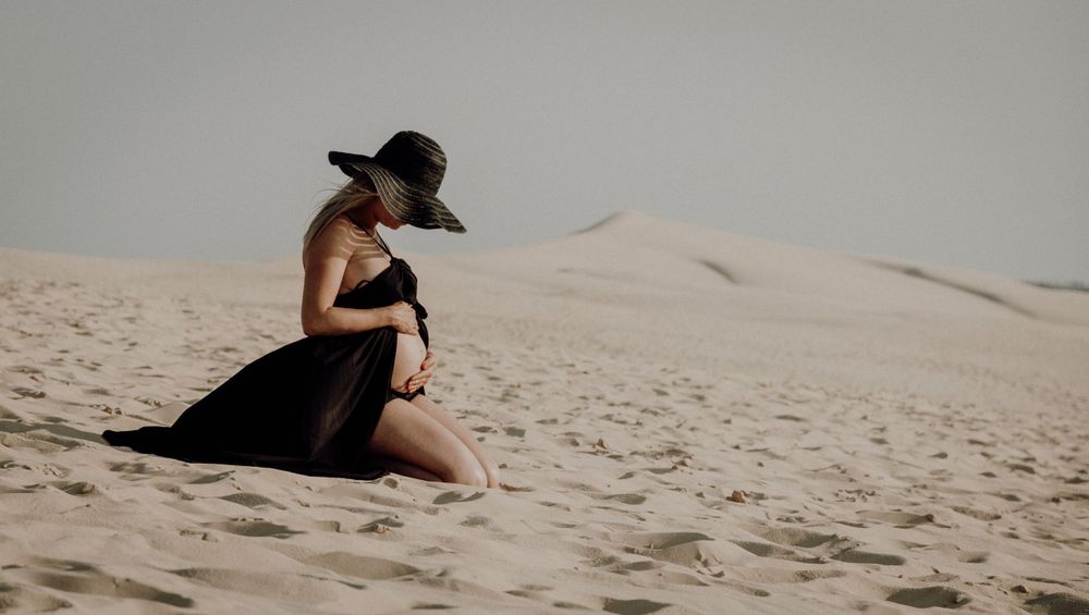 Person sitting alone on sandy dunes during golden hour. photographe futur maman Bordeaux gironde