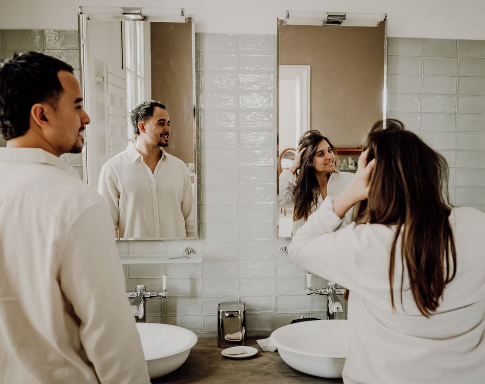 Couple getting ready together in a white tiled bathroom with dual mirrors and sinks. photographe futur maman Bordeaux, Gironde