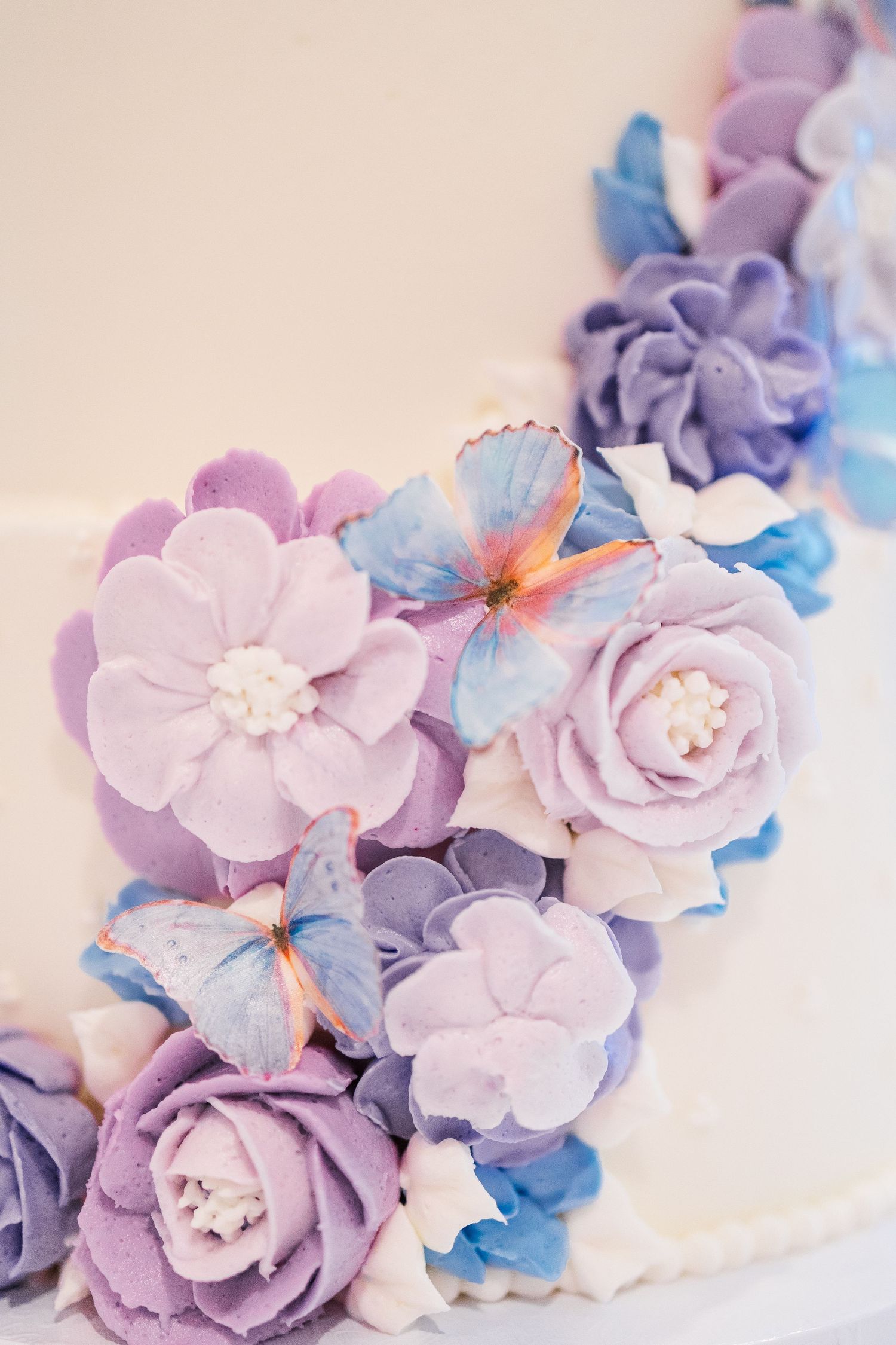 Beautiful purple and blue sugar flowers with butterflies decorate a wedding cake detail.