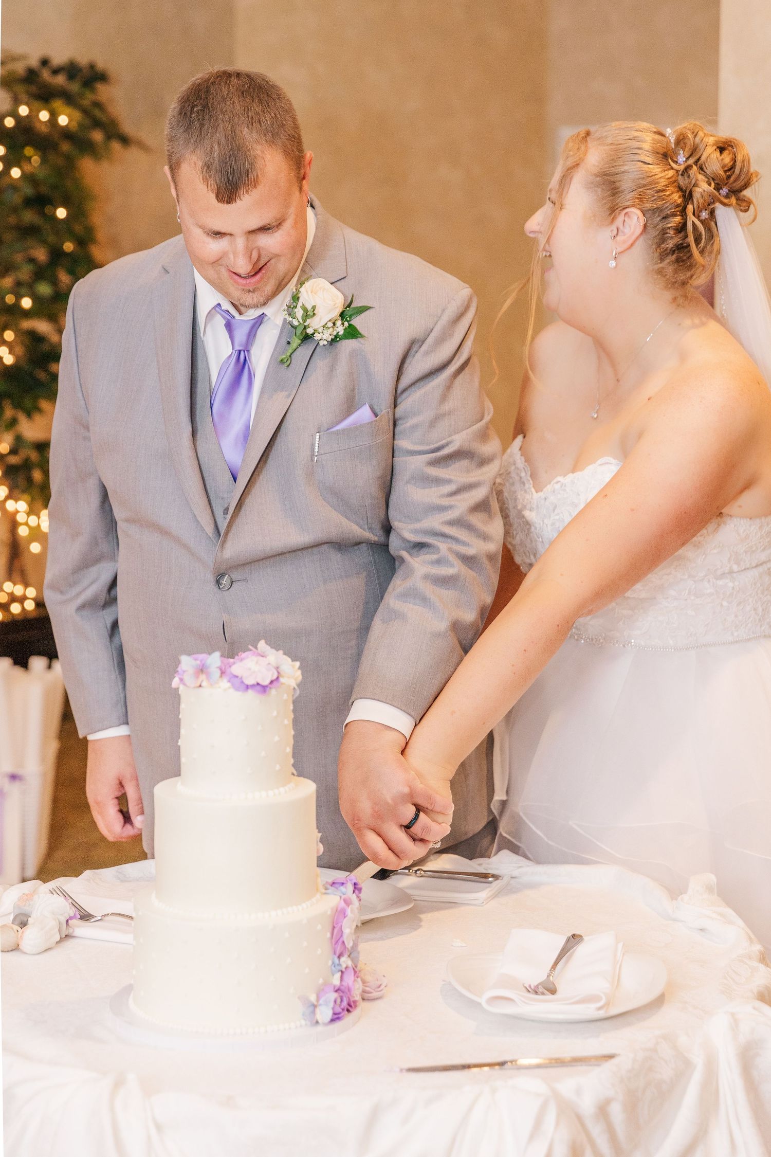 Newlyweds share a moment while cutting their white tiered wedding cake.