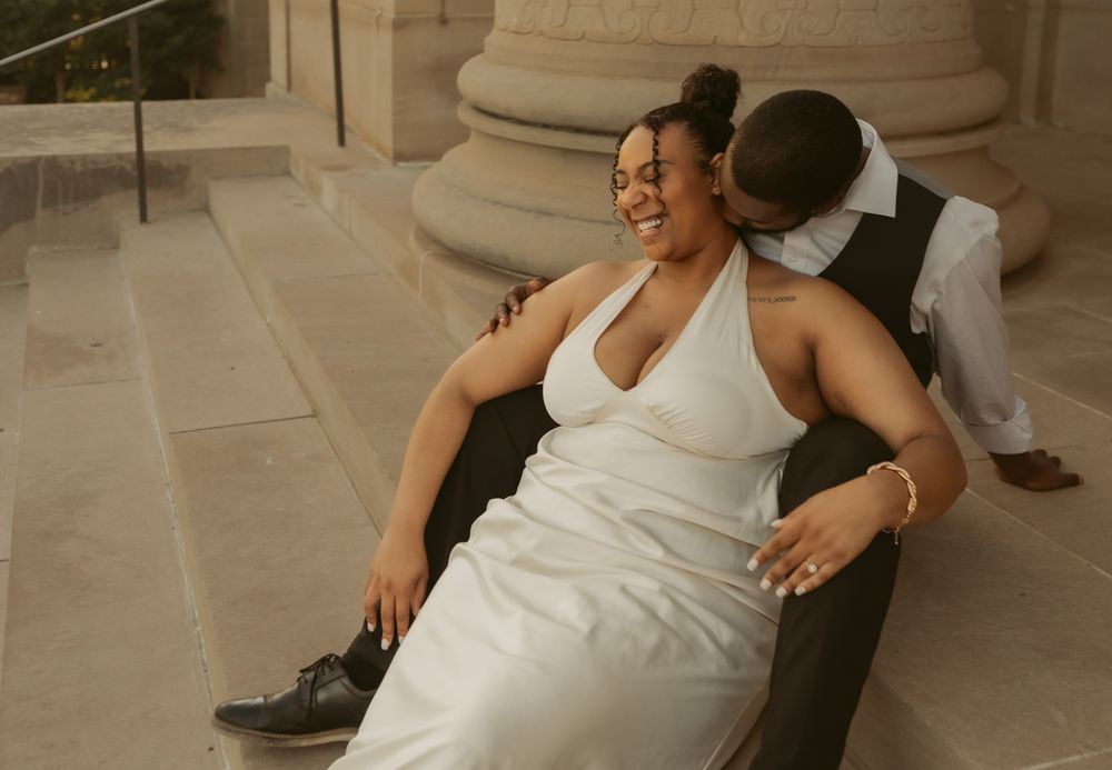 A joyful couple shares an intimate moment while posing by stone columns in wedding attire.