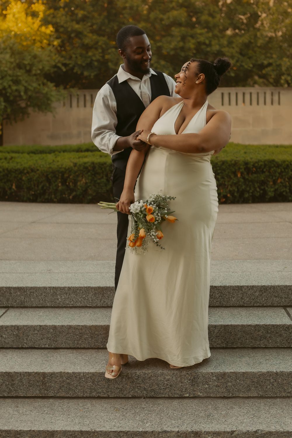 Joyful couple shares a romantic moment on stone steps with autumn foliage in the background during their wedding day.