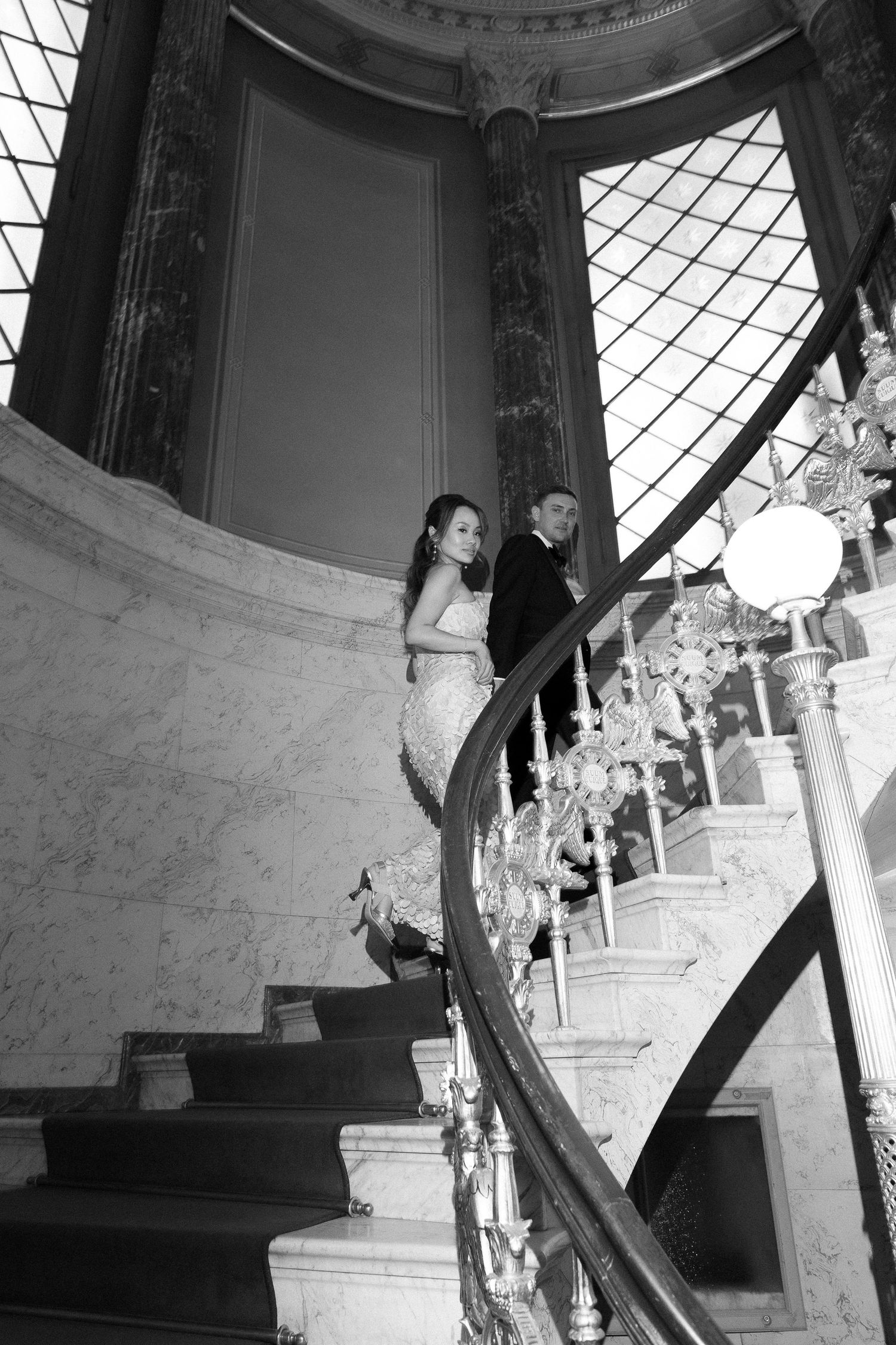 A couple ascending an ornate stone staircase, with the bride wearing a flowing white gown trailing behind.