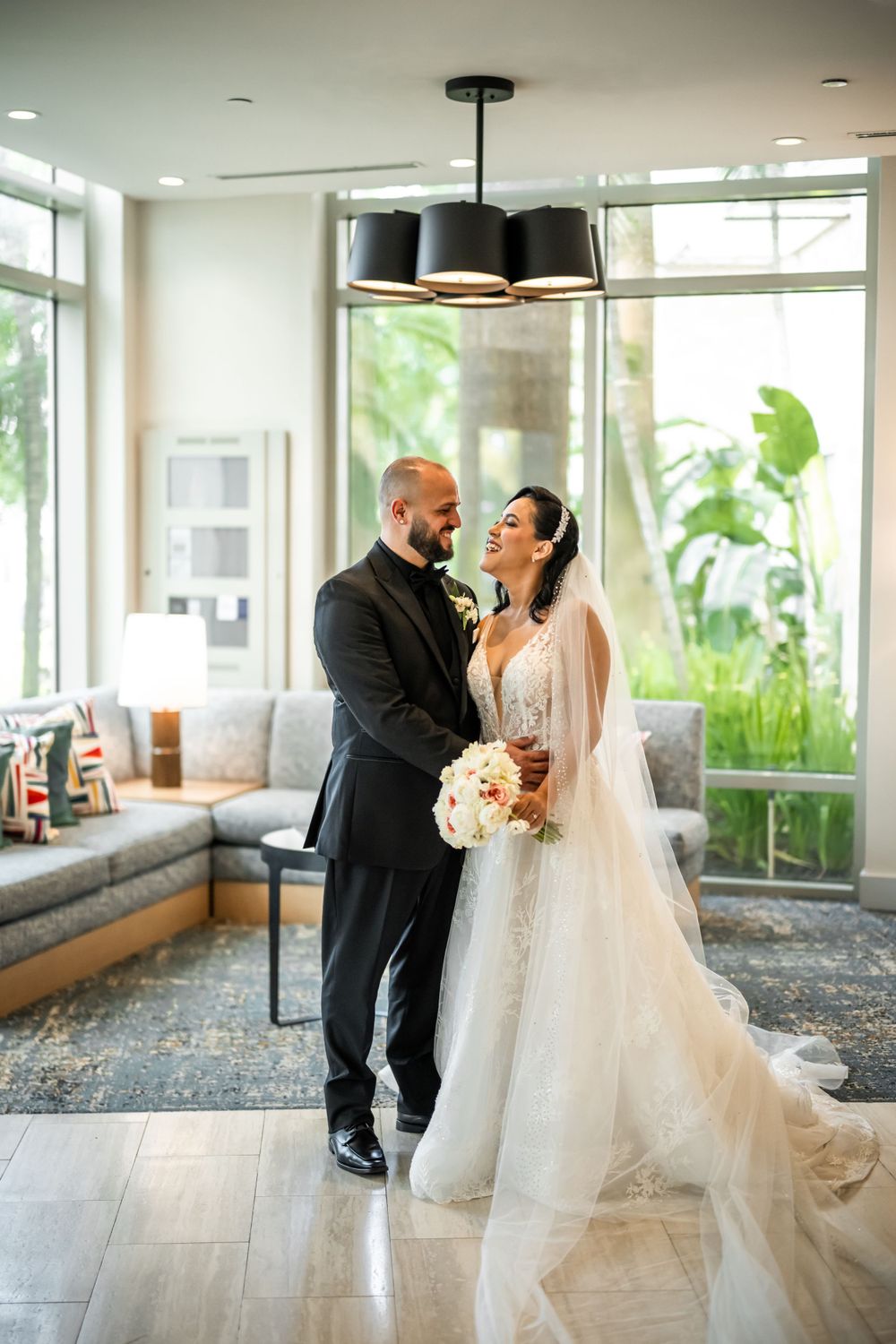 A romantic wedding portrait shows the newlyweds sharing a joyful moment in an elegant room with natural light.