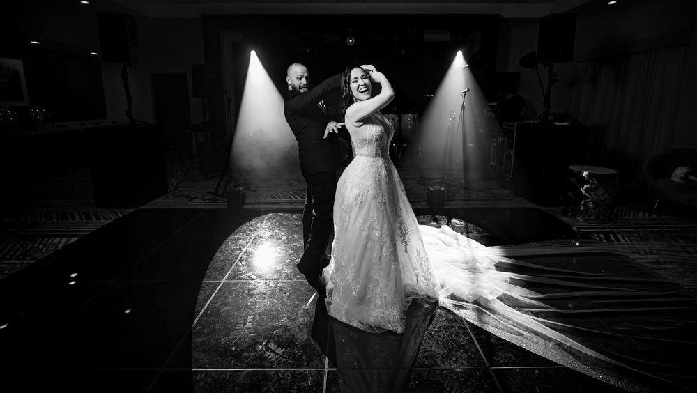 An artistic black and white wedding photo captures the couple's dance with dramatic spotlighting.