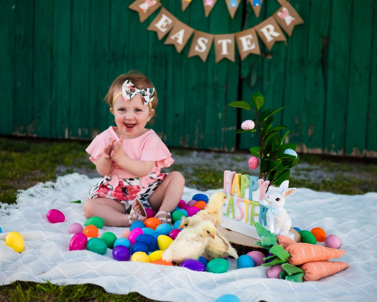 Easter celebration setup with colorful eggs and decorations against a green fence.