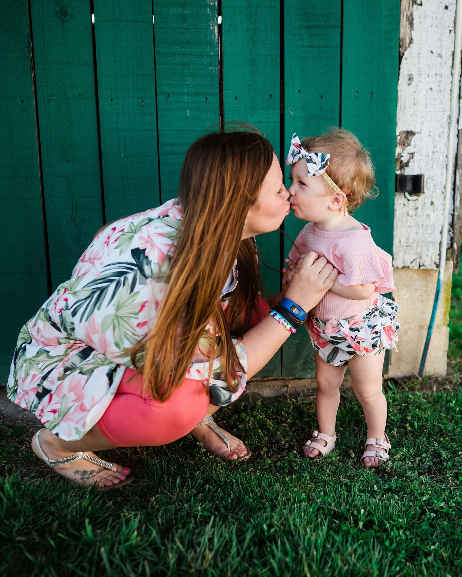 A sweet moment shared against a green wooden fence background.