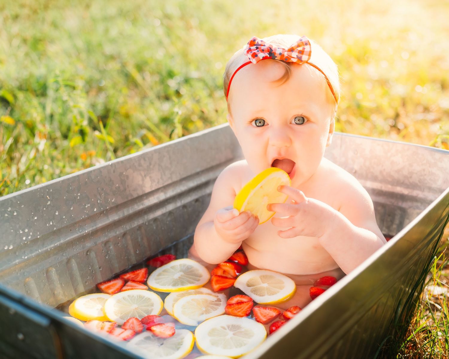 Baby splashing and playing in vintage metal tub during golden hour outdoor photo session.