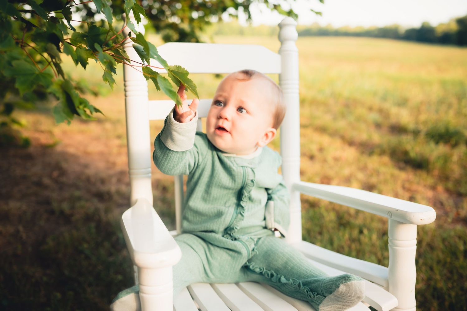 Baby in mint green outfit plays on white wooden bench outdoors.
