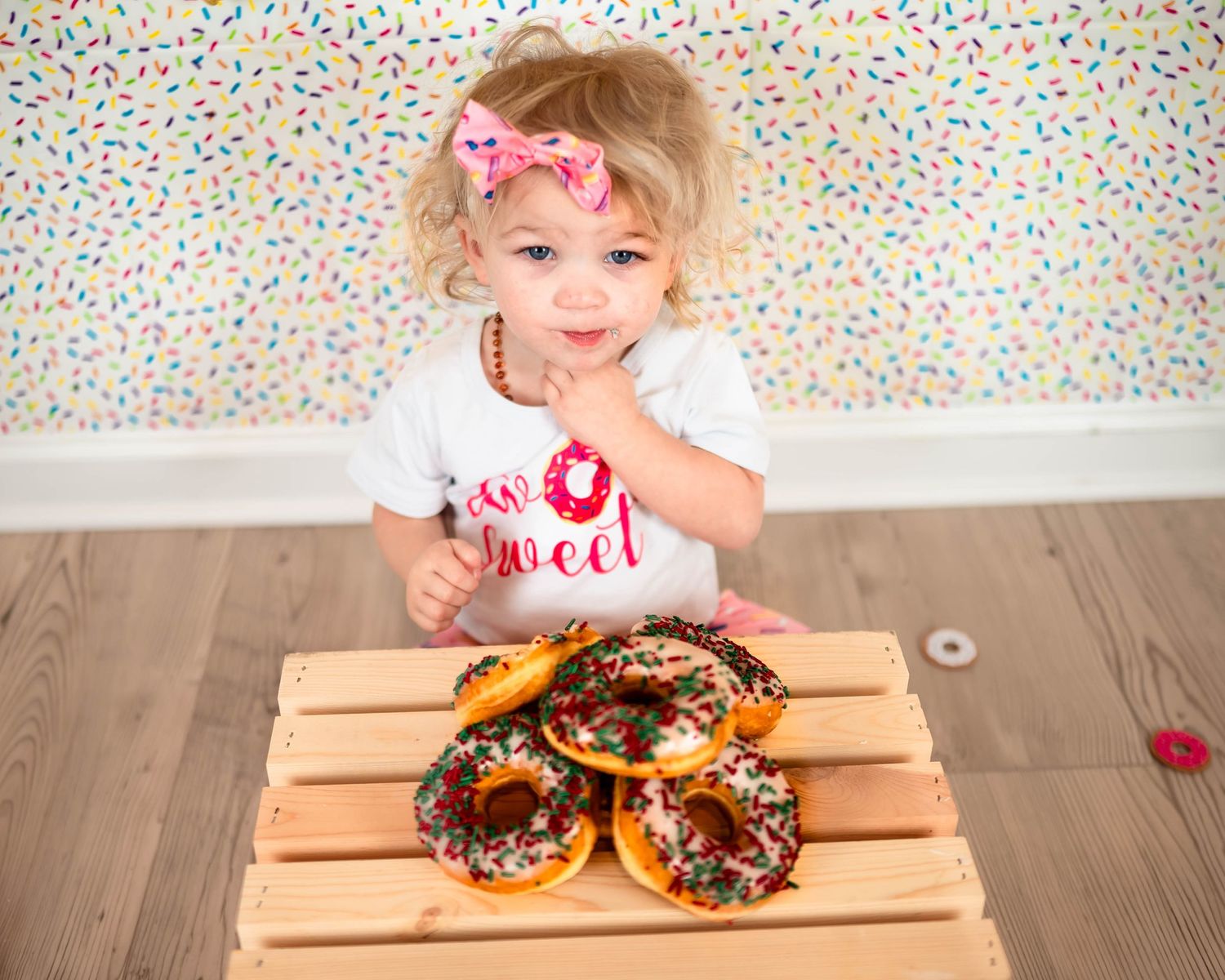 Colorful sprinkle background with donuts and wooden box setup for a festive photo session.