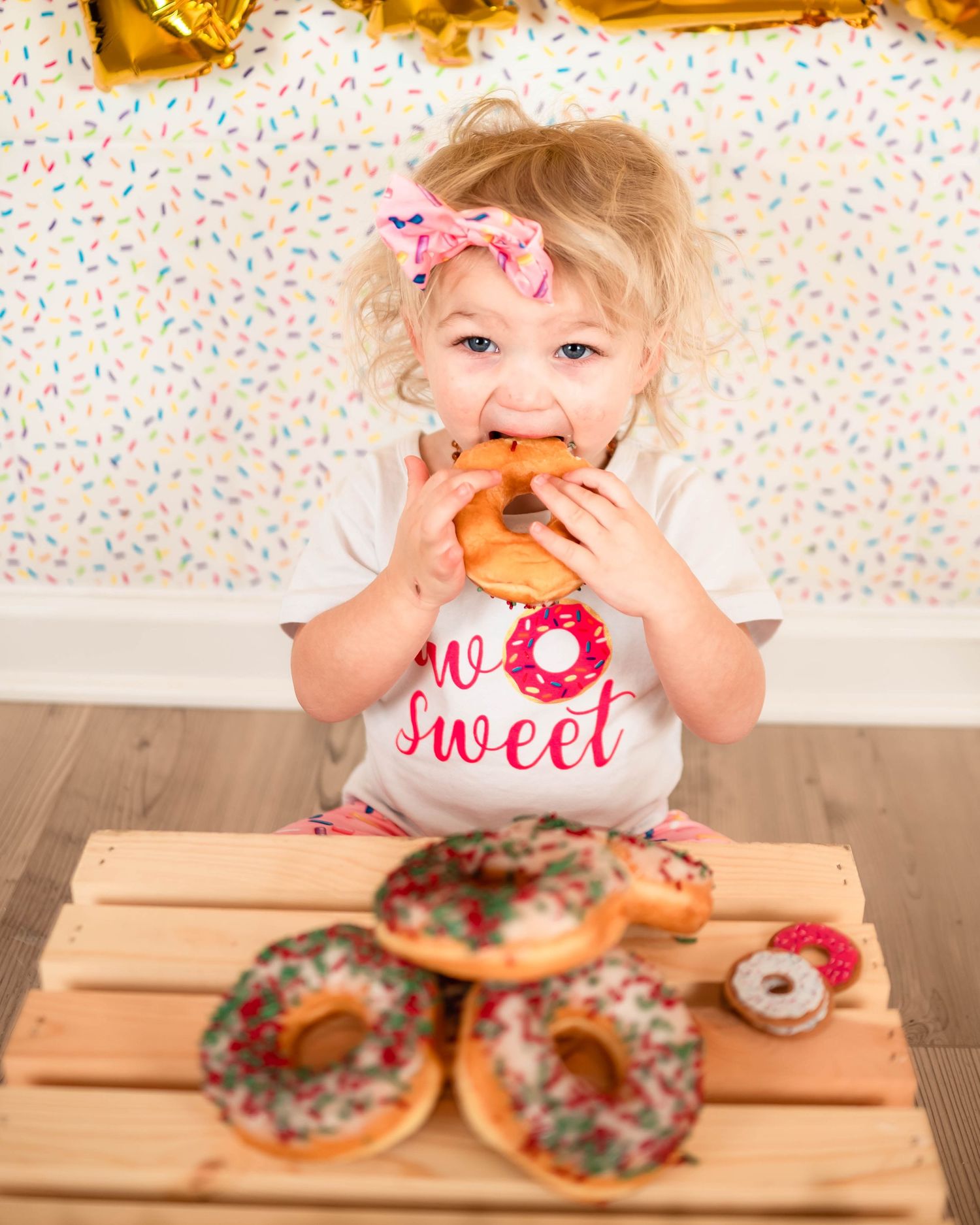 Decorated donuts arranged on a wooden box against a sprinkle-patterned backdrop.