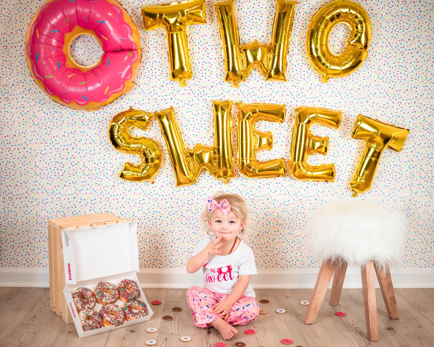 Birthday setup with pink donut and gold letter balloons spelling TWO SWEET.