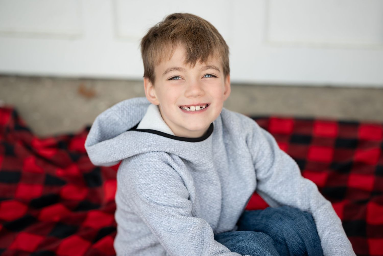 Siblings in casual winter outfits pose playfully on a red and black checkered blanket.