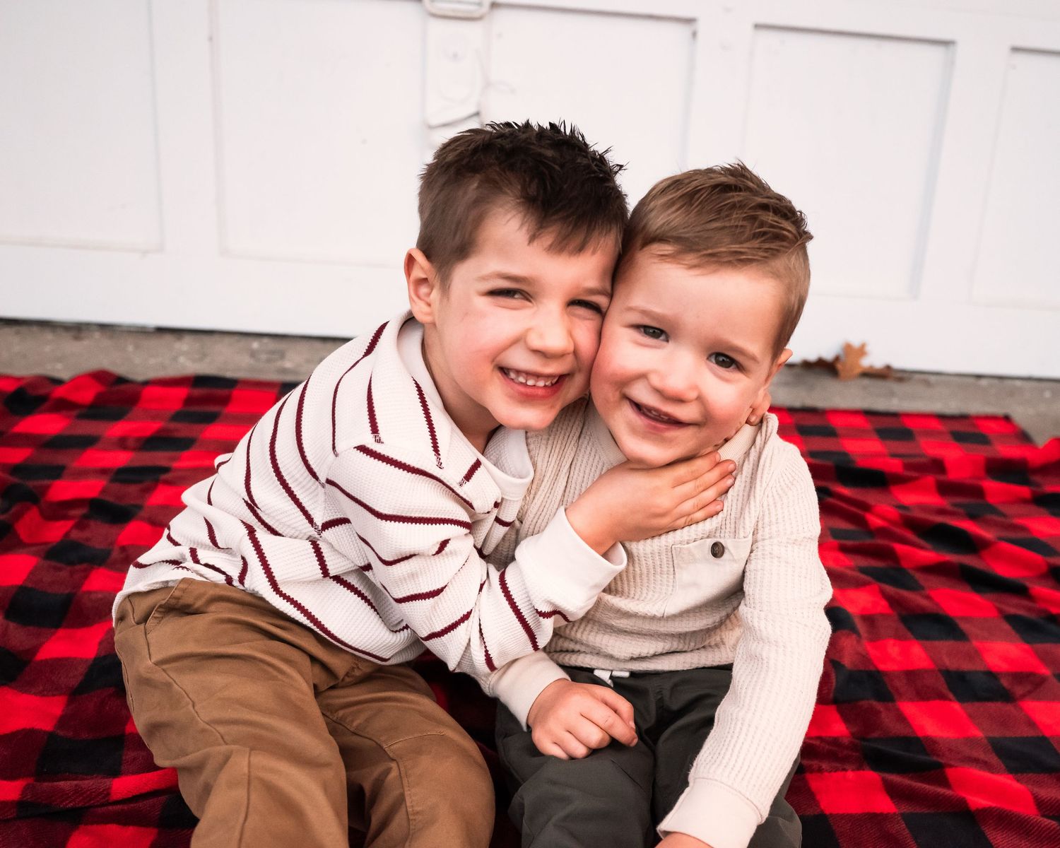 Two children laughing and playing together on a red and black buffalo plaid blanket.