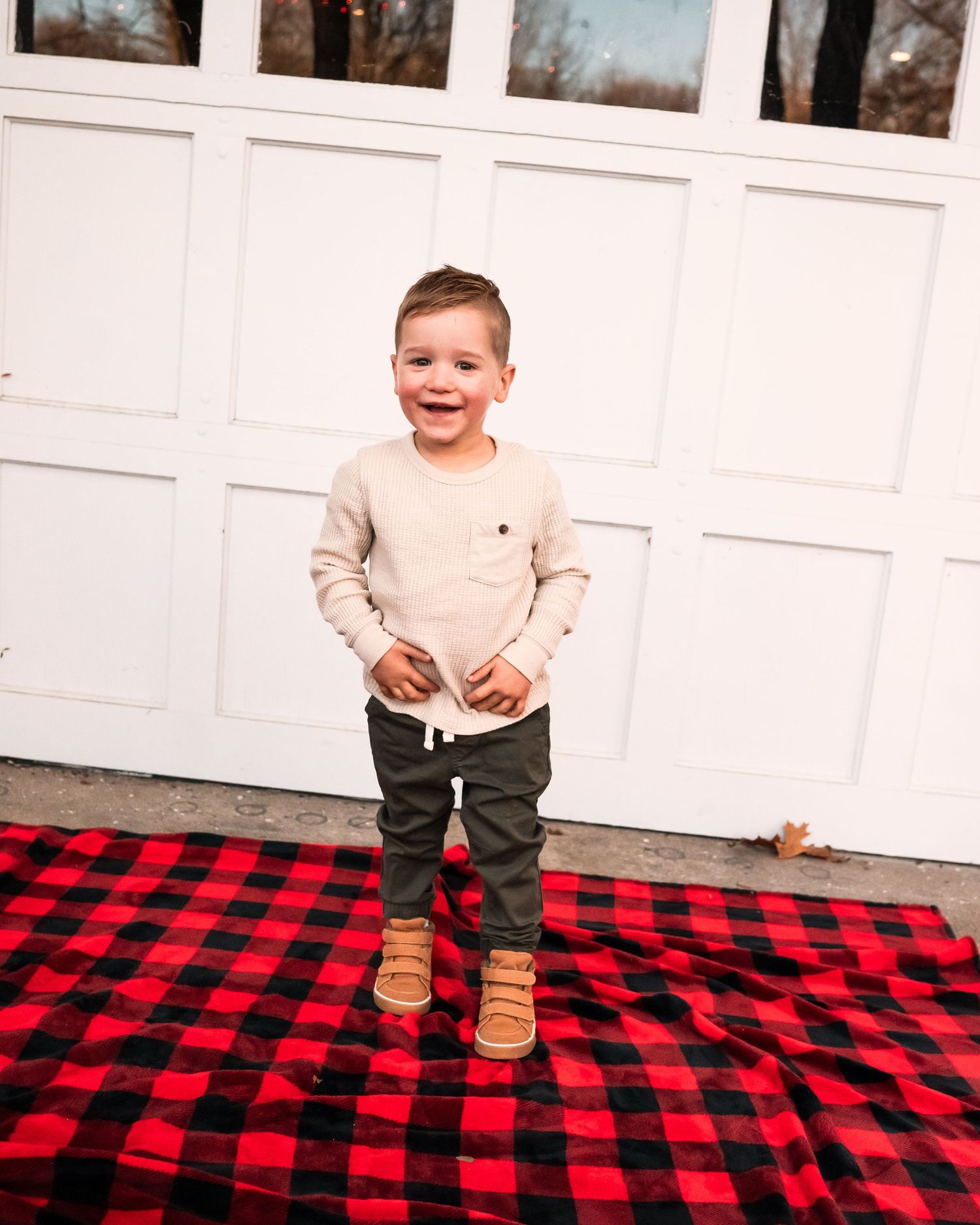 A child sits and laughs on a cozy red and black buffalo plaid blanket outdoors.