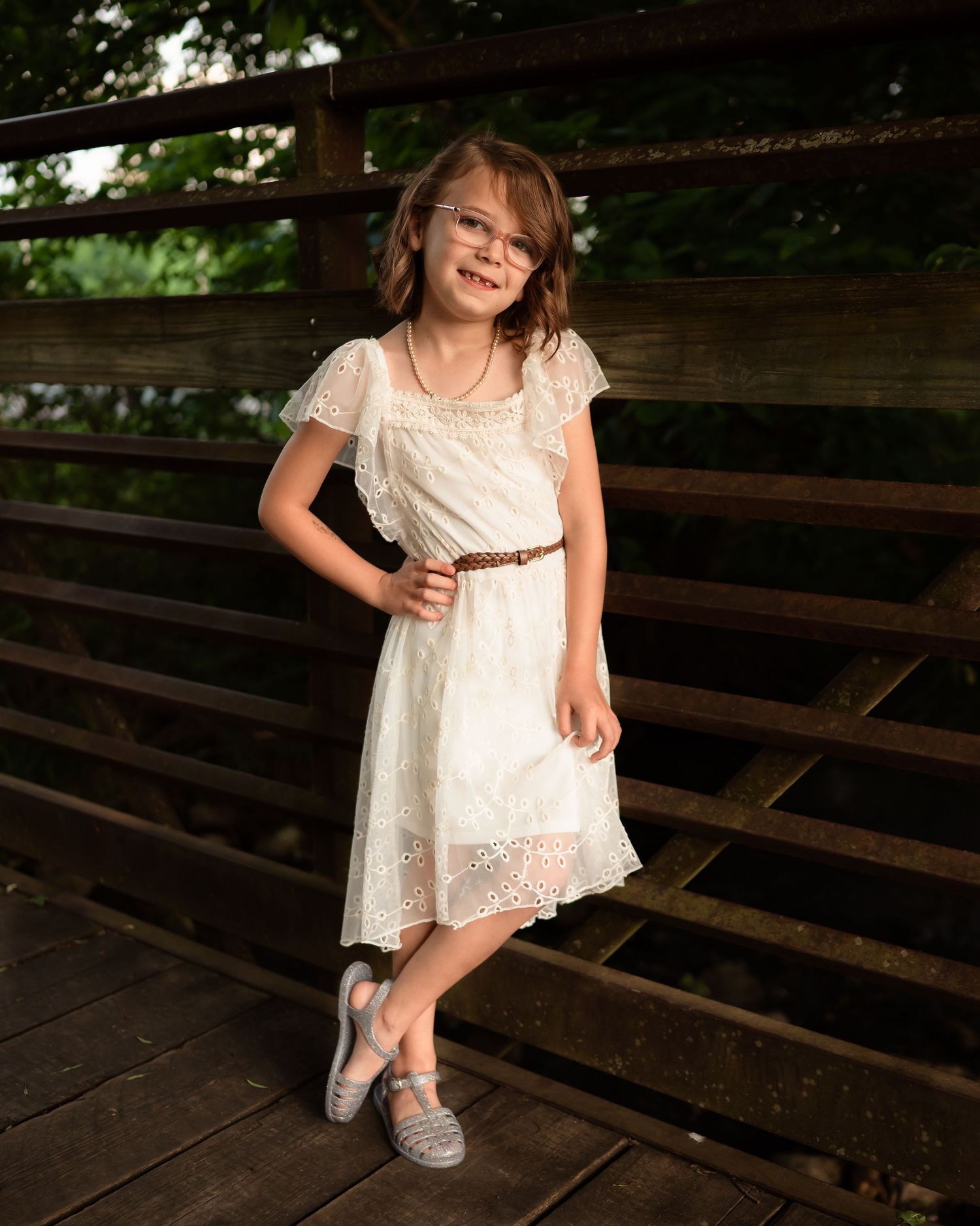Child in white dress posing on rustic wooden deck.