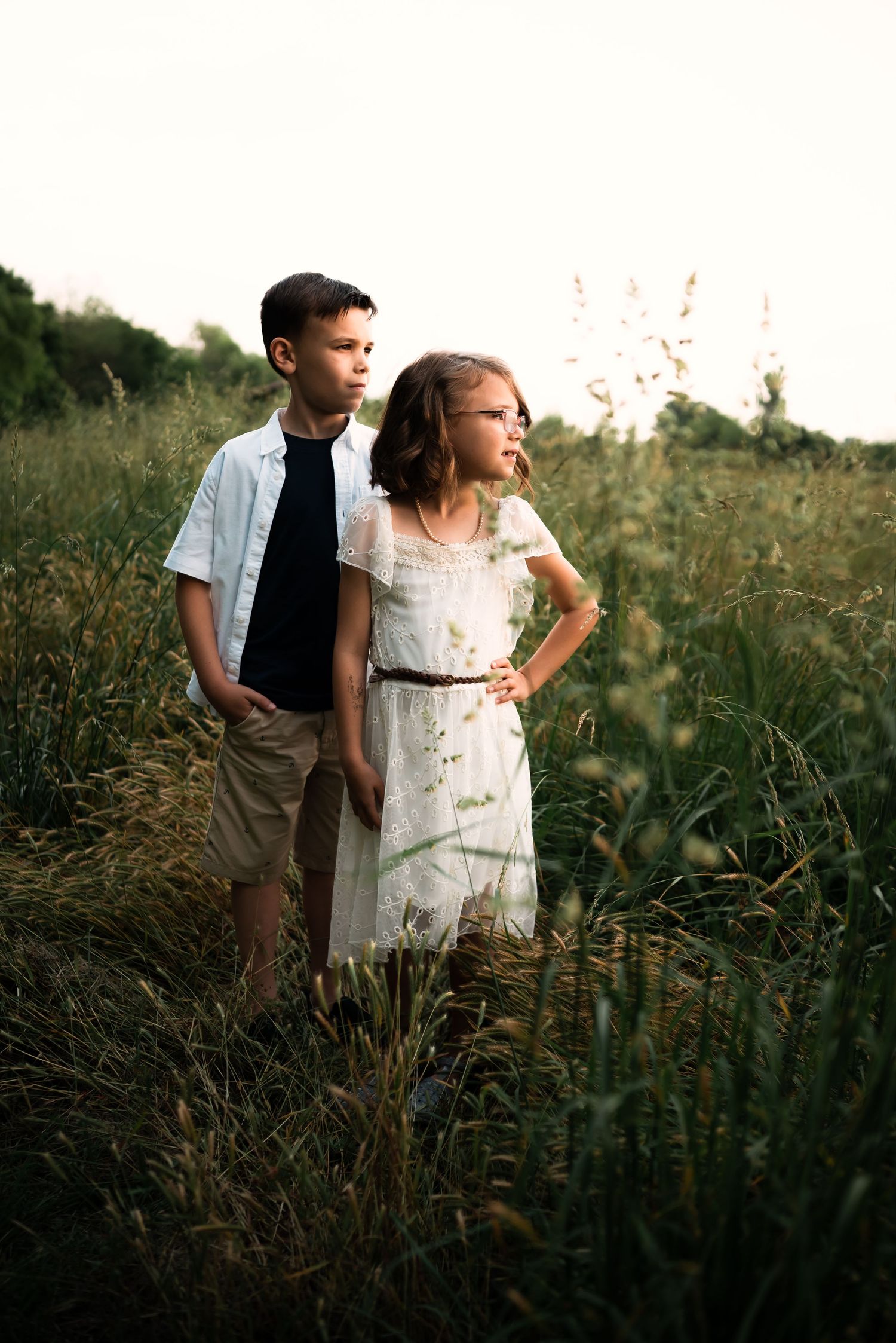 Two figures stand in a golden field at sunset wearing casual summer attire.
